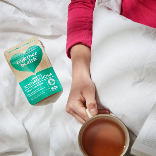 Lady in bed holding a cup of tea and a packet of tablets.