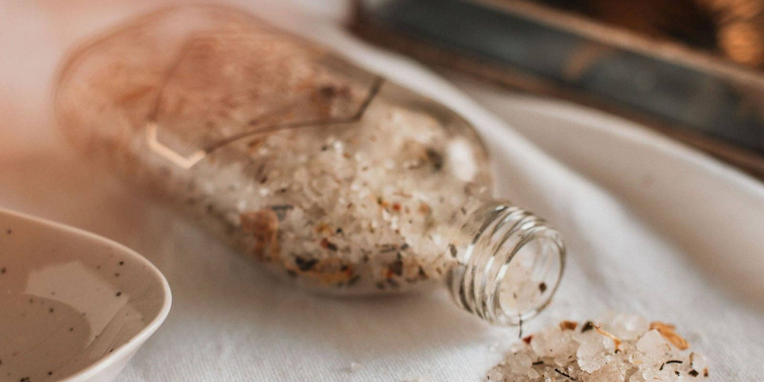 salts spilling out of jar onto a tablecloth. With a dish and a tray in background.