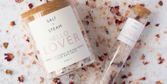 A jar and a refill tube of salts laying on a bed of salt and rose petals.