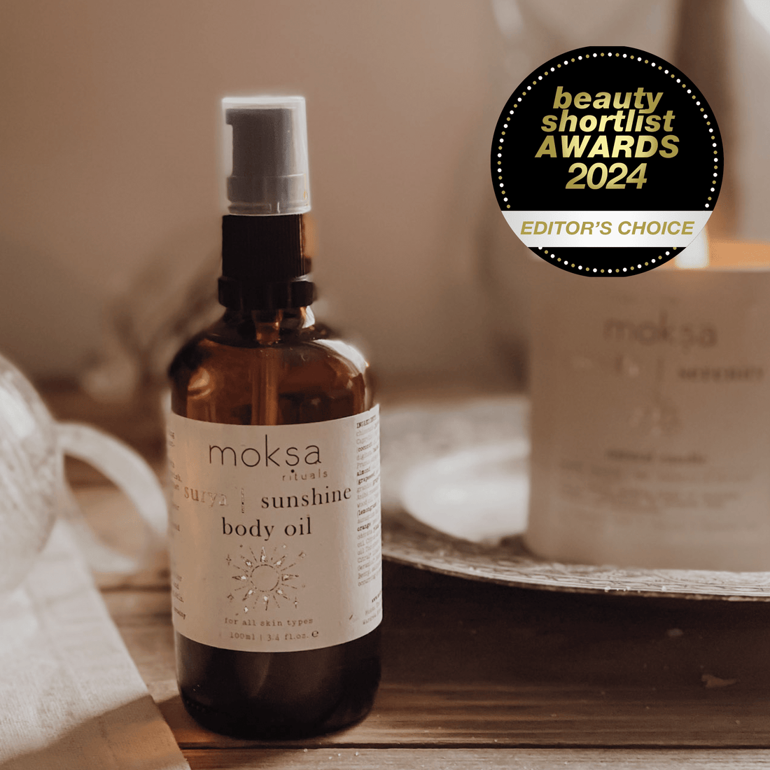 Bottle of body oil on a wooden table with a candle in the background. Also an award sticker in the corner.