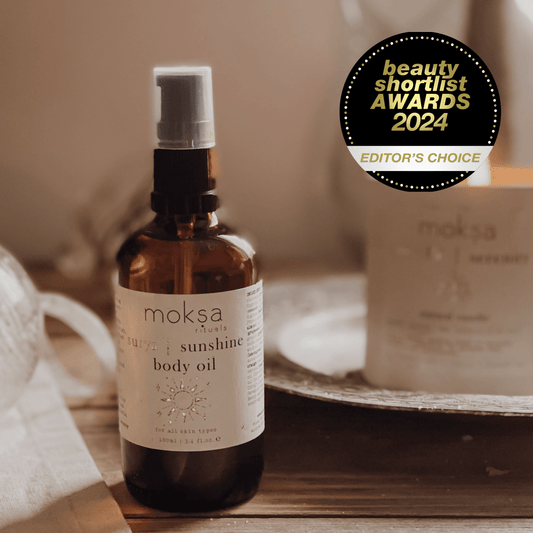 Bottle of body oil on a wooden table with a candle in the background. Also an award sticker in the corner.