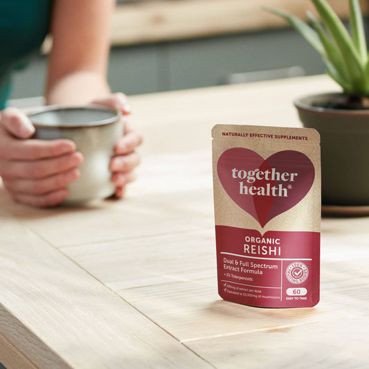 Packet on mushrooms on a table, with a set of hands holding a mug in background and a plant on a table.