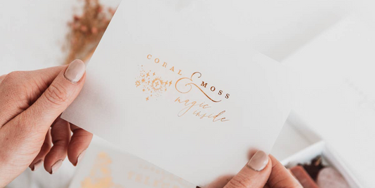 A gift set and a branded card being held by a pair of hands from Coral and Moss