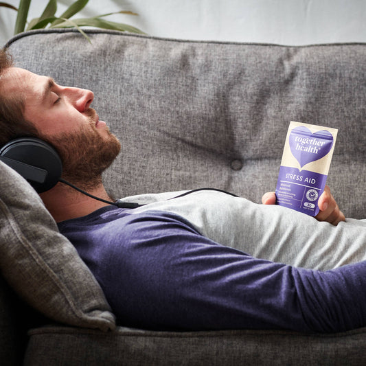 Man laying on sofa with headphones on holding a packet of Stress Aid Vitamins.