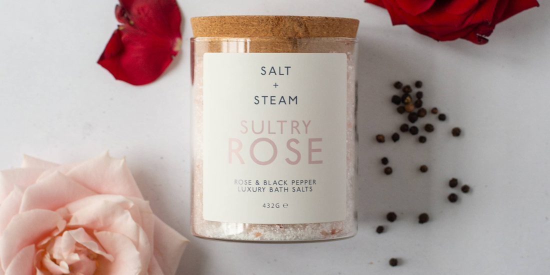 Bath salt jar with rose scattered rose petals and peppercorns.