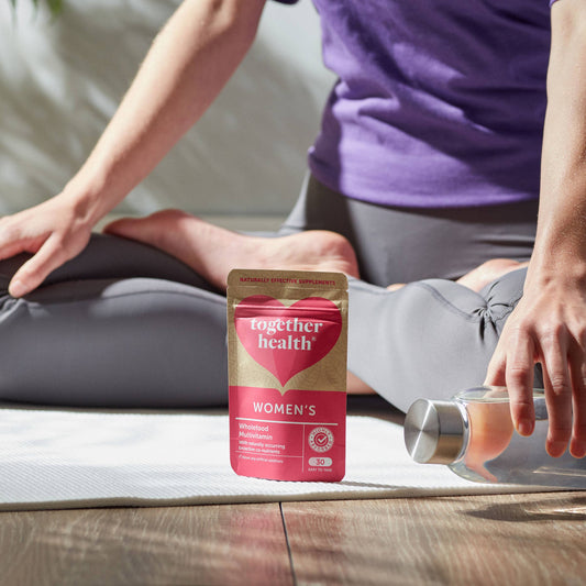 Women in a yoga pose with a packet of tablets and a bottle of water.