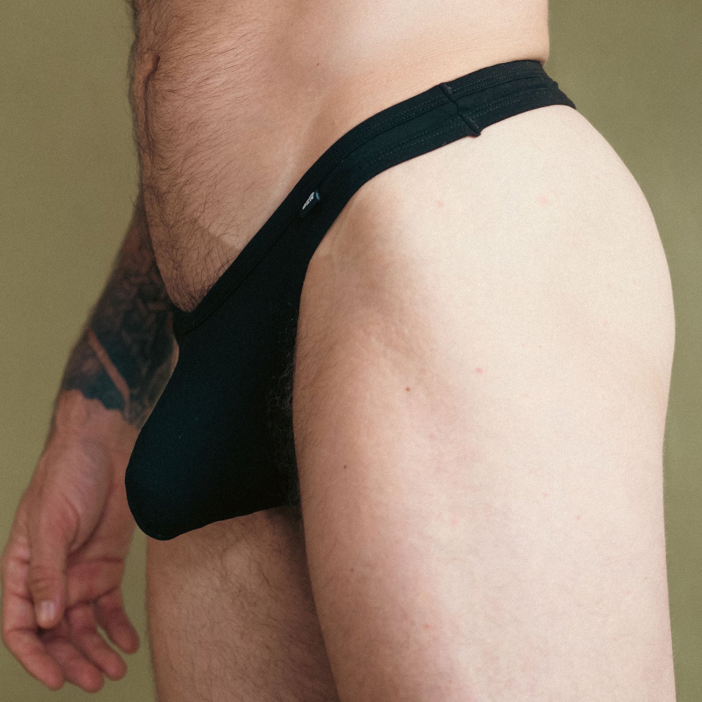 Man wearing a black thong against a green background