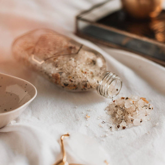 salts spilling out of jar onto a tablecloth. With a dish and a tray in background.