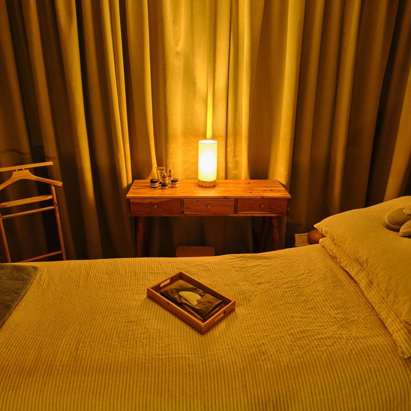 Bedroom with a wooden nightstand, lamp, and decor items against a curtain backdrop.
