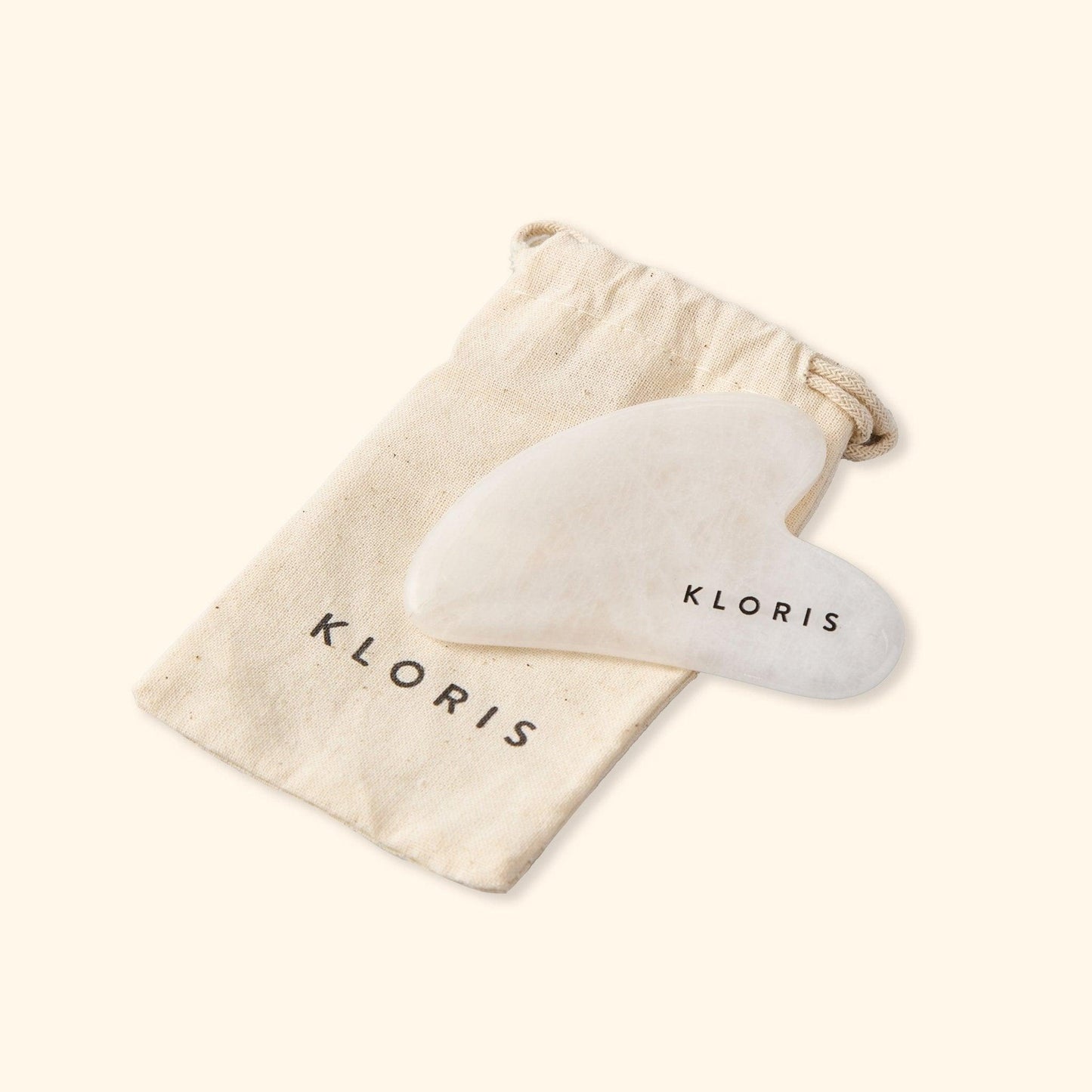 White Gua Sha tool with 'KLORIS' branding on a matching drawstring bag.