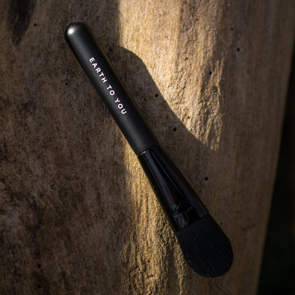 Black makeup brush with 'Earth to You' branding on a textured stone background