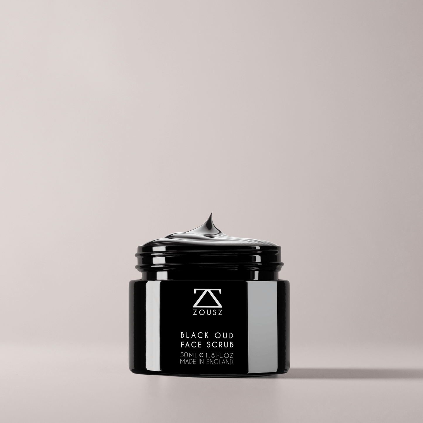 Black jar of ZOUSZ Black Oud Face Scrub on a light gray background