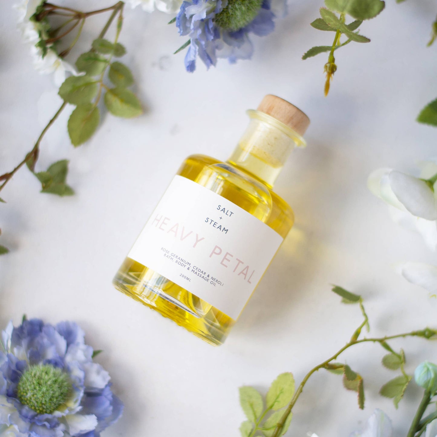 Bottle of Floral Body, Bath and massage Oil on a cloth with flowers around it.