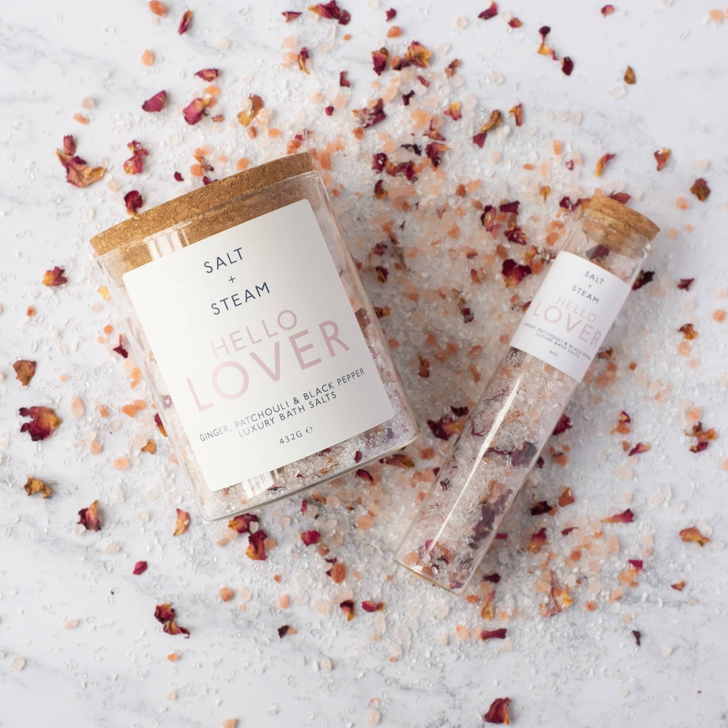A jar and a refill tube of salts laying on a bed of salt and rose petals.