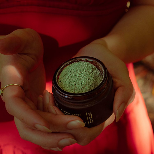 Person holding a jar of green powder with a red background