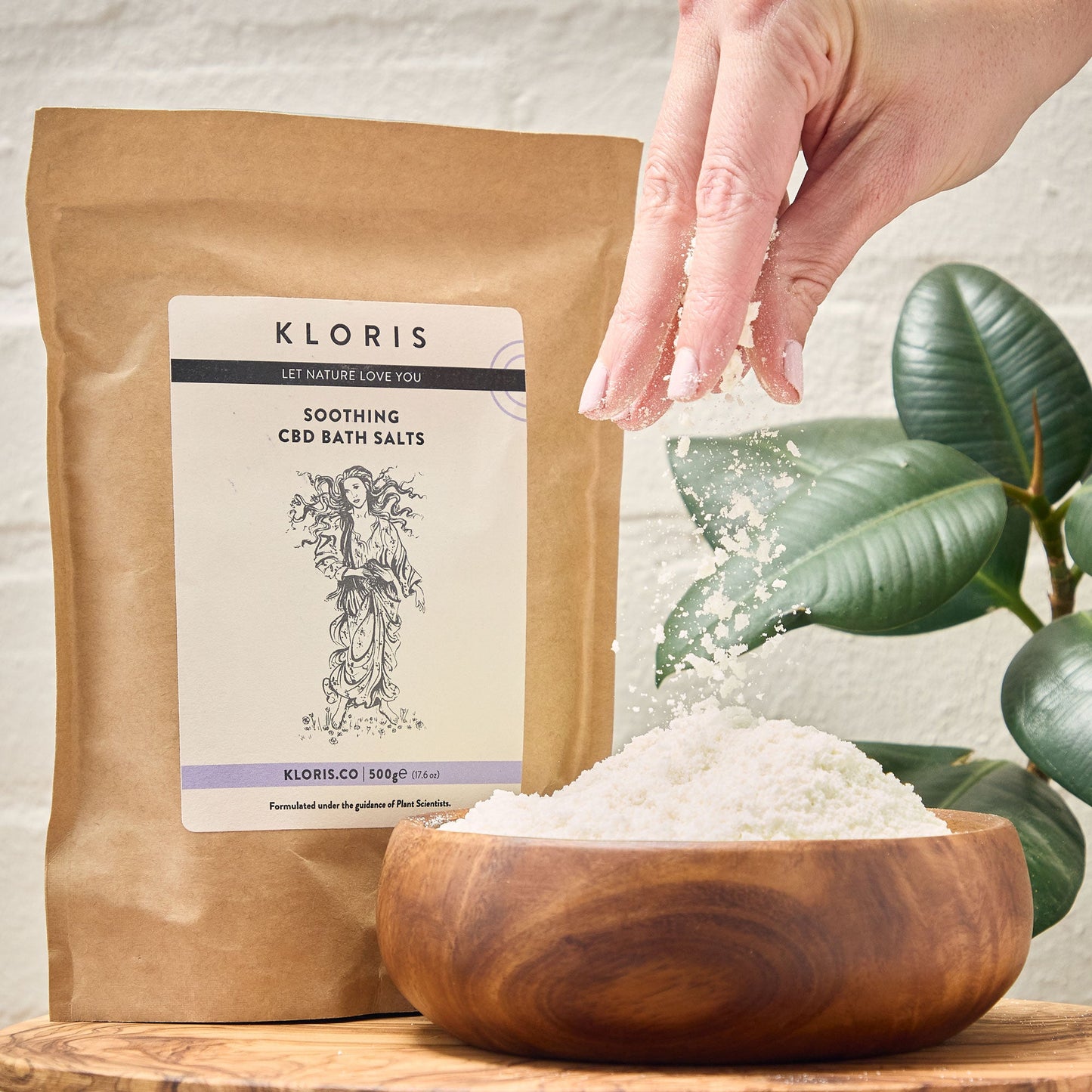 Kloris CBD bath salts packaging with a wooden bowl of bath salts and a hand holding a pinch.
