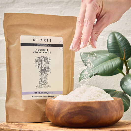 Kloris CBD bath salts packaging with a wooden bowl of bath salts and a hand holding a pinch.