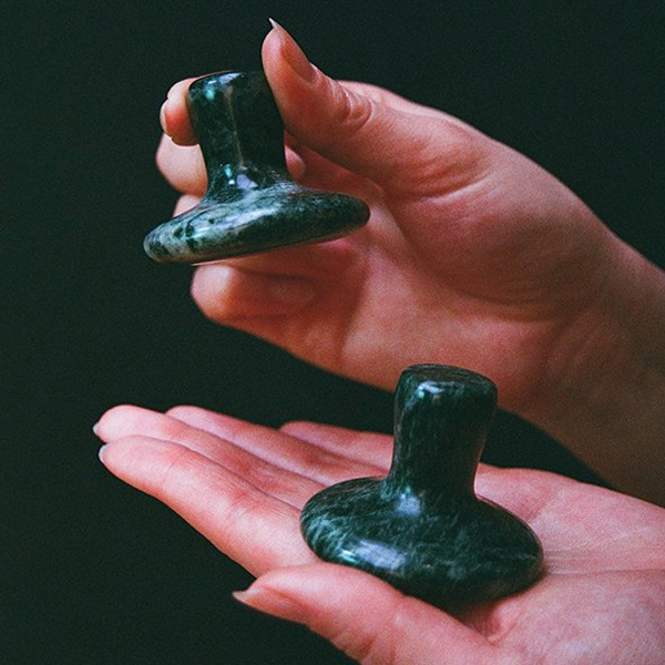 Two green stone objects held in hands against a dark background