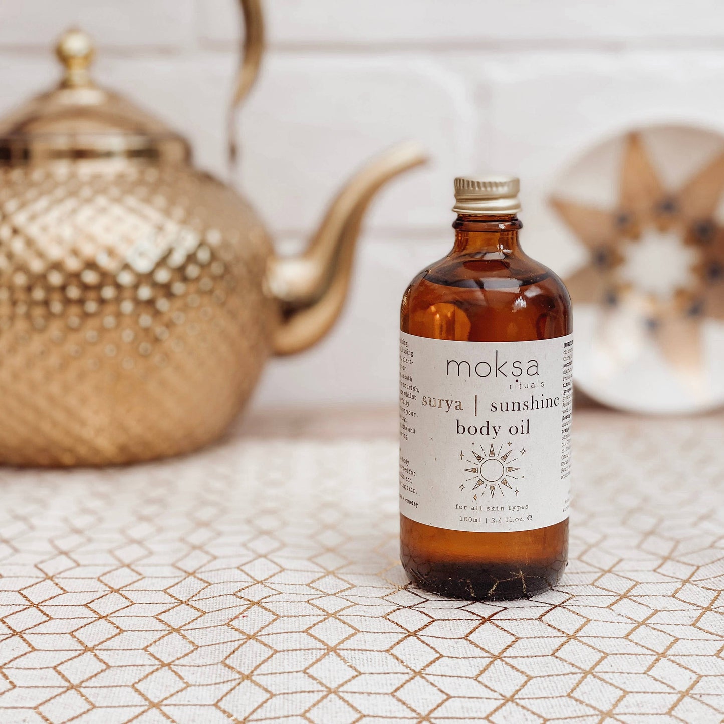 Bottle on a printed table, with a star plate and a gold kettle in the background.