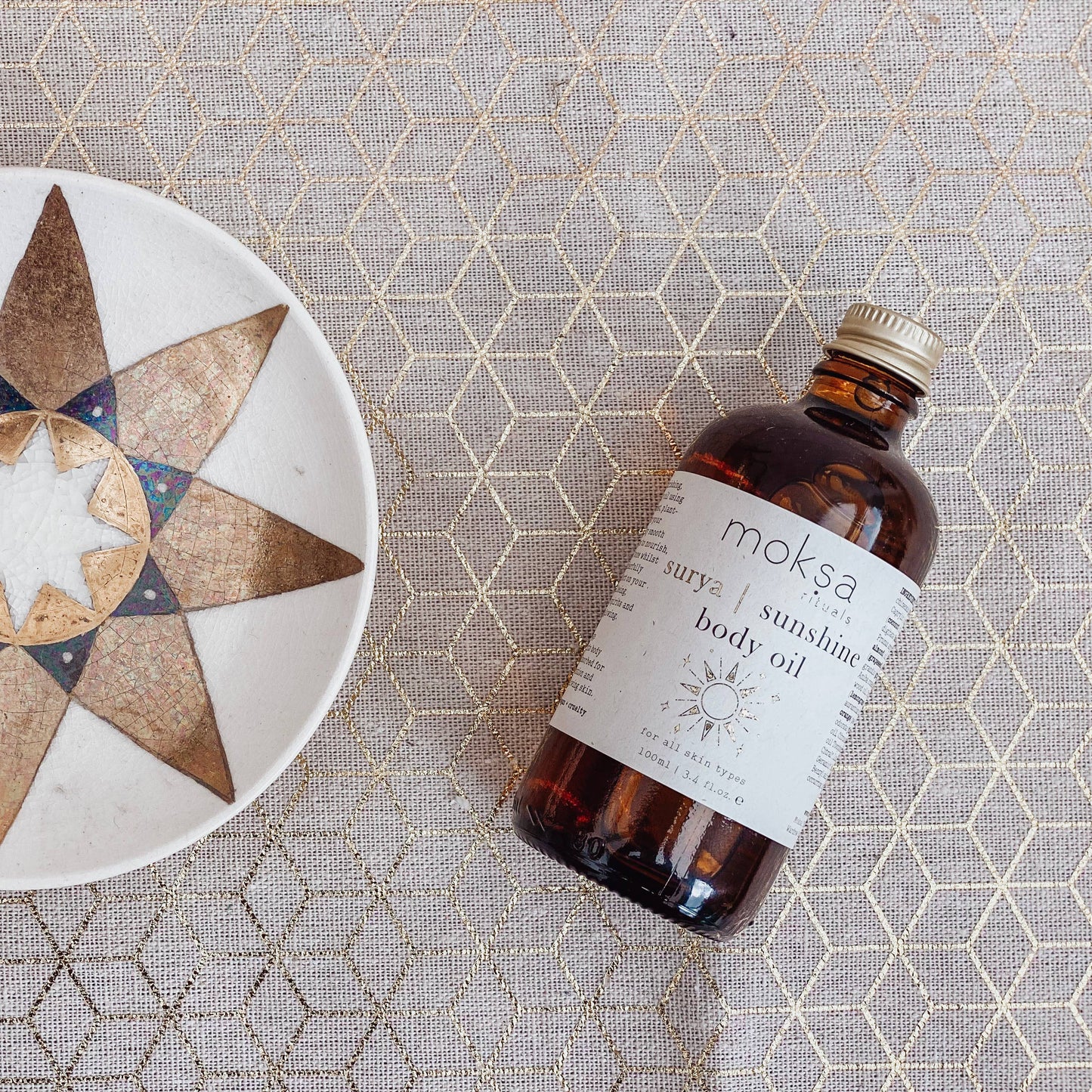 Bottle laying on its side on a printed table cloth next to a star plate.