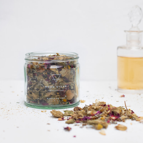 Glass jar of dried herbs with 'Moon Steam' branding on a light background