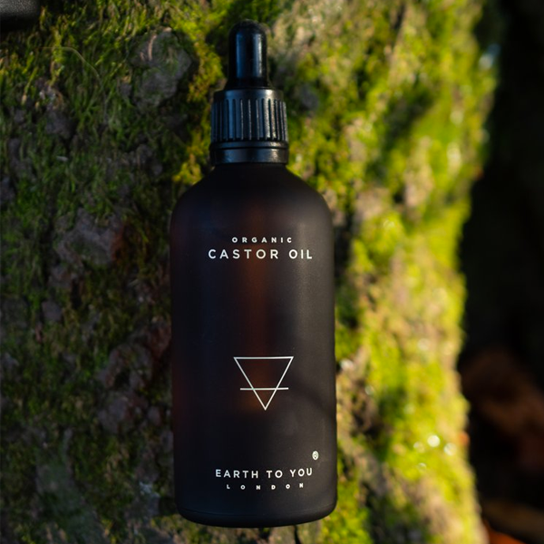 Black bottle of organic castor oil with a dropper on a textured green background
