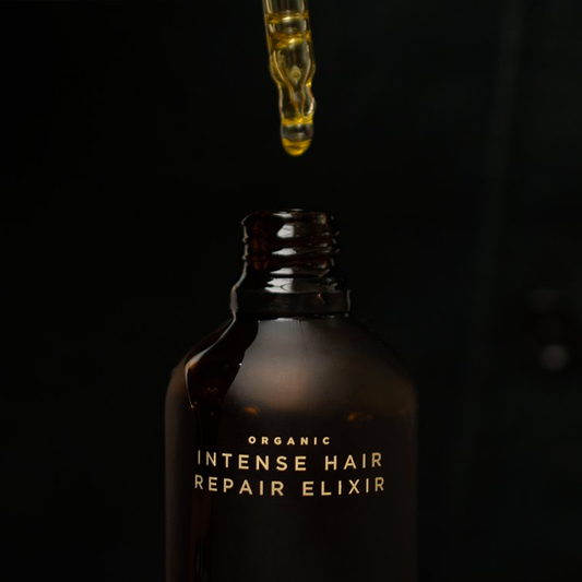 Bottle of 'Organic Intense Hair Repair Elixir' with a dropper above it on a dark background