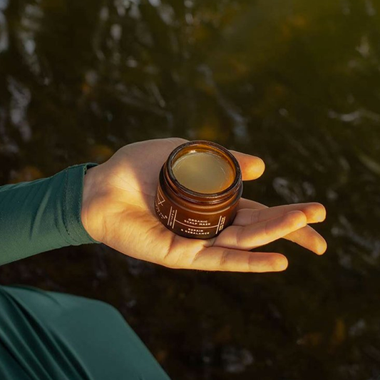 Hand holding a small brown jar with a blurred natural background