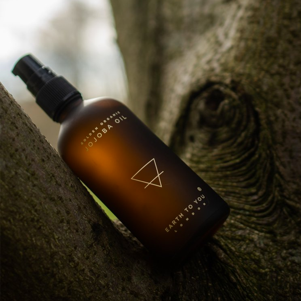Bottle of jojoba oil with a black spray nozzle on a textured surface