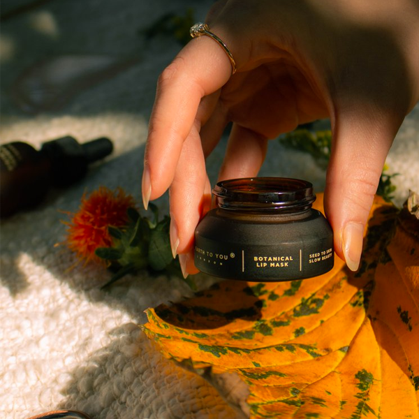 Person holding a black lip mask jar with floral and natural elements in the background