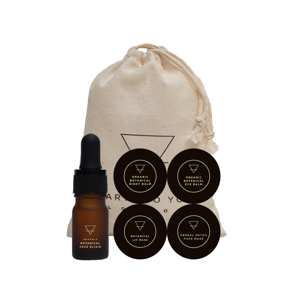Skincare set with a dropper bottle, face mask, and lip balm in a drawstring bag on a white background