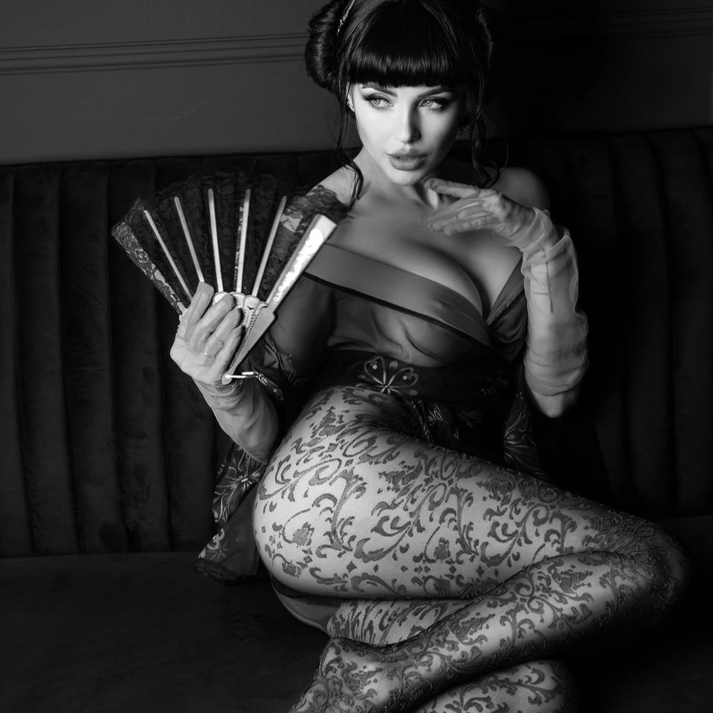 lady with asian hair piece and fan, wearing red tights and lace chemise sitting on sofa.