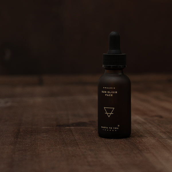 Black bottle labeled 'Sun Elixir Face' on a wooden surface with a dark background