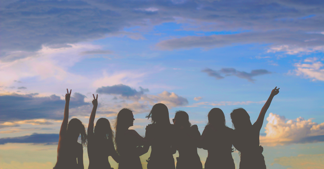 7 women celebrating with their hands waving in front of a skyline