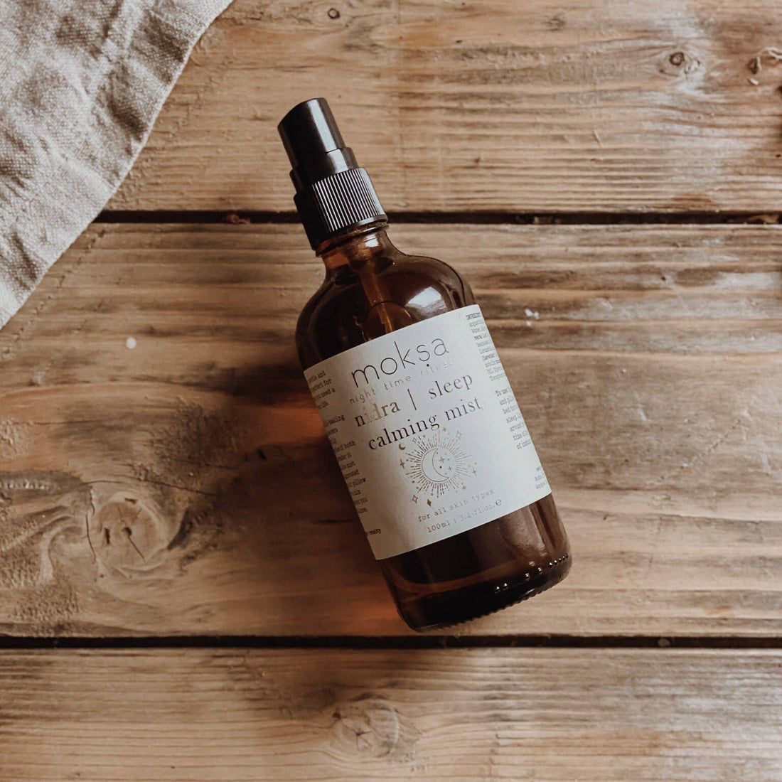 Bottle laying down on a wooden table with some cloth to the side.