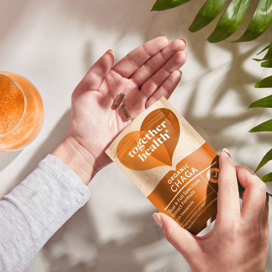 Packet of tablets being shaken into the palm of a hand.  Glass of juice and  plant in the picture.