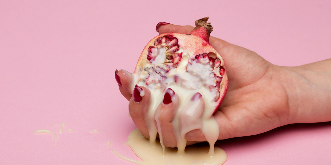 A hand holding a cut open Pomegranate covered in custard.