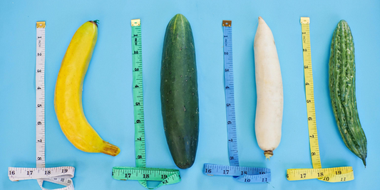 Tape Measures laying next to a banana, cucumber, and some root vegetables.