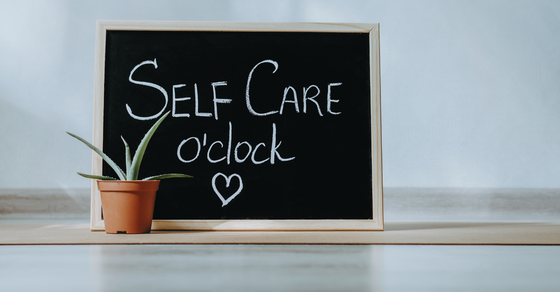 self care written on blackboard on table with a plant next to it