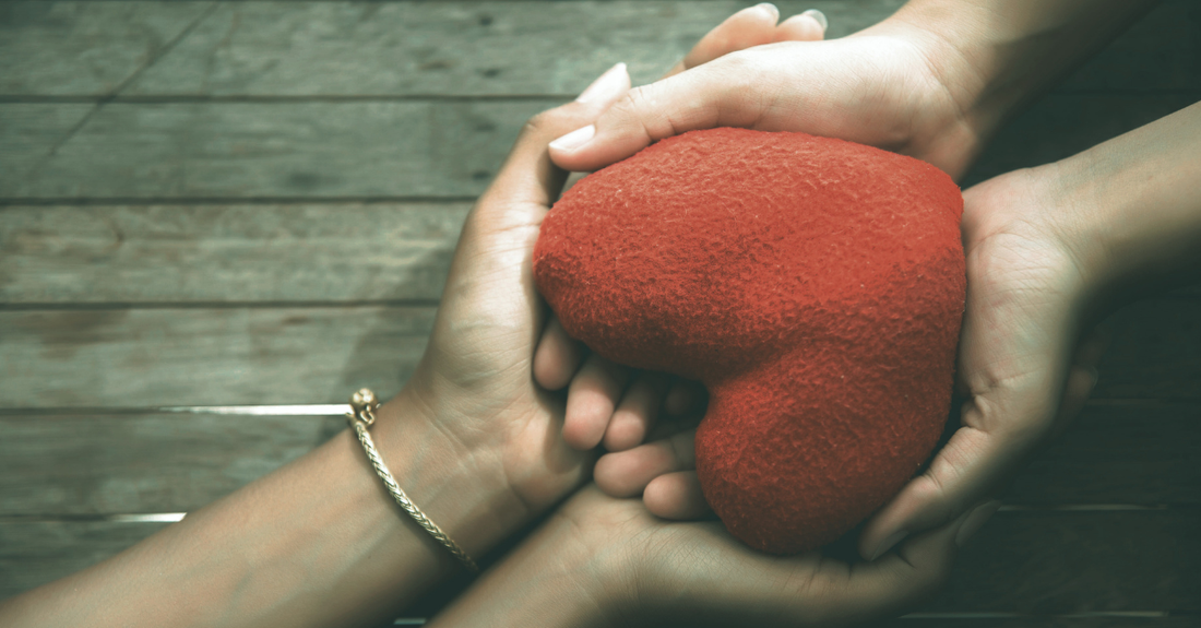w hands holding a heart on a wooden background
