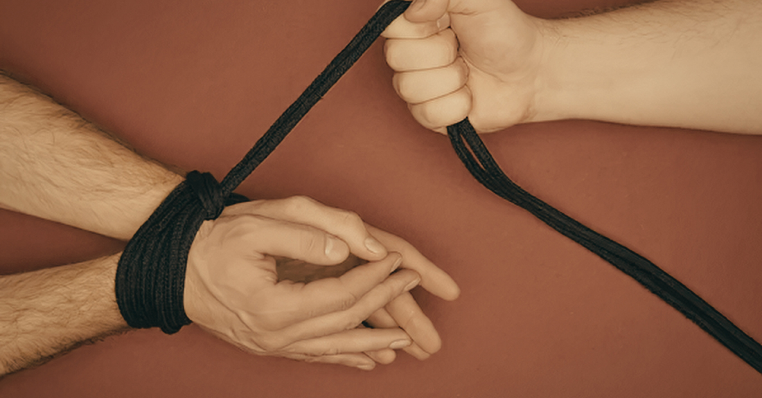 lady holding rope tied around mans wrists on red background.