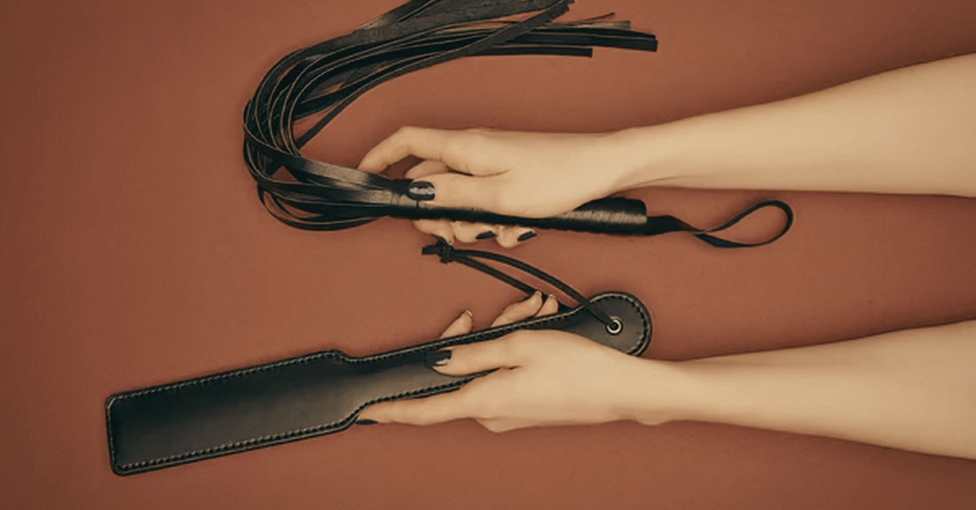 a lady holding a paddle and a whip on a red background.
