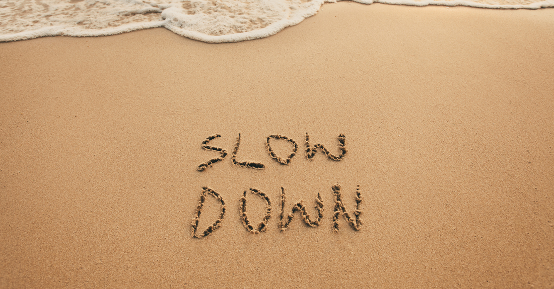 the words slow down written in the sand on the beach