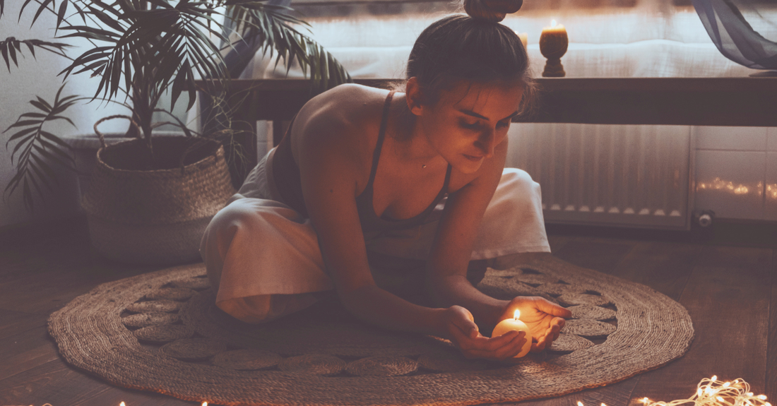 lady meditating with a candle sitting on a rug with plants in background