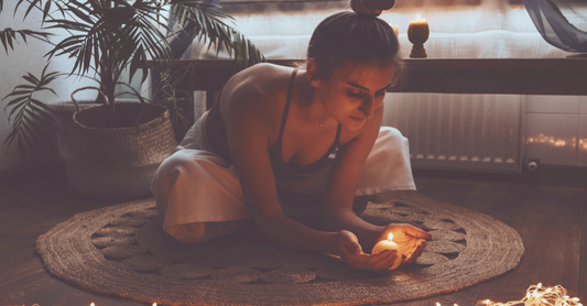 lady meditating with a candle sitting on a rug with plants in background