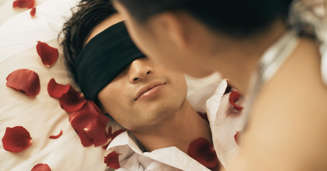 man in blindfold in bed with women and roses on bed