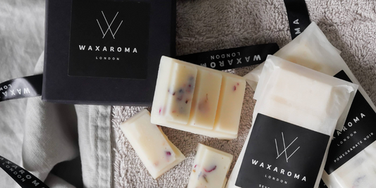 Two Waxaroma packets and one open melts bar on a towel and blanket with eucalyptus leaves and a Waxaroma branded box