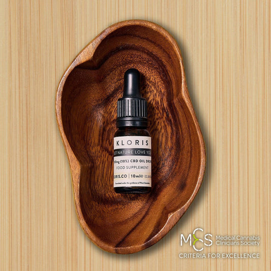 Bottle of KLORIS CBD oil dropper on a wooden surface with 'MCS Medical Cannabis Clinicians Society' logo.