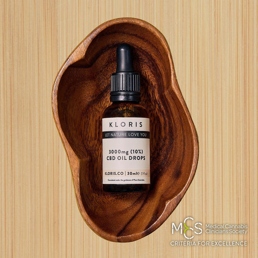 CBD oil bottle labeled 'KLORIS' in a wooden dish on a wooden background
