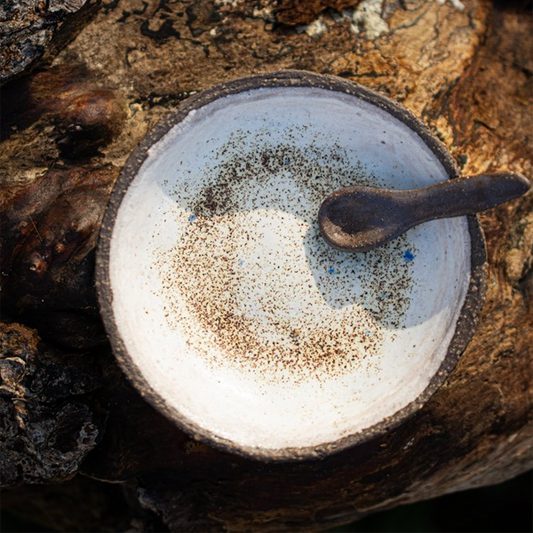 White ceramic plate with a black rim on a wooden surface, featuring a small black spoon.